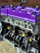 complete engine on display with purple rocker cover with brick background