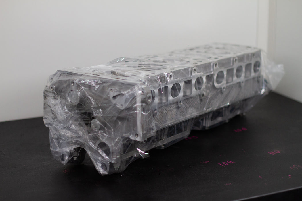 engine cylinder head wrapped in plastic on a black bench with a white background