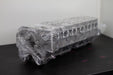 engine cylinder head wrapped in plastic on a black bench with a white background